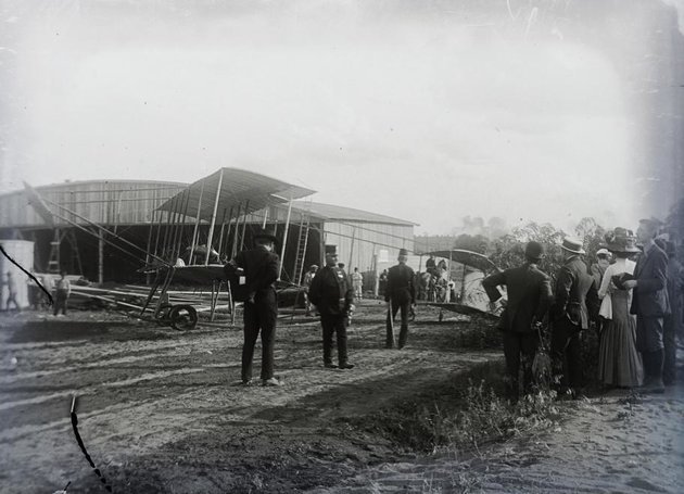 Farman gép a hangárok egyike közelében az érdeklődők kis csoportjával (kép forrása: Fortepan/ Magyar Műszaki és Közlekedési Múzeum / Archívum / Negatívtár / Tas Gyula gyűjteménye)