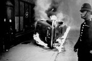 Rendőr áll egy égő autó mellett, amelyet egy kelet-londoni kommunista tüntetés alatt gyújtottak fel, 1936.