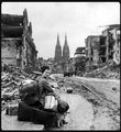 Otthontalanná váló német lány üldögél csomagjaival a sáros utcán, miután egy intenzív szövetséges légitámadás letarolta városát (1945)