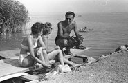 Miközben az úr a parton a hölgyeknek udvarol, a háttérben egy fiú ejtőzik gumimatracán a Balatonban (1961) 