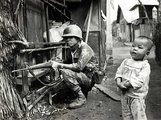 Egy kíváncsi gyermek áll egy dél-vietnámi katona mellett Saigon egyik külvárosában, amelyet Vietkong gyanúsítottakat keresve kutatnak át a dél-vietnámi és amerikai erők (kép forrása: historycentral.com)