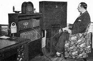Hugo Gernsback New York-i otthonában egy korai televízió-készülékkel 1928-ban. A készülék felső részén látható lyukban van elhelyezve a másfél col (kb. 3,8 centiméter) átmérőjű képernyő, amelynek a hanghoz történő szinkronizálását Gernsback a kezében tartott irányítóval maga végzi (kép forrása: Wikimedia Commons)