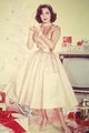 Elizabeth Taylor, 1950 – a kor egyik legnagyobb nevű színésznője egy ünnepi reklámfotózáshoz aranyszínű szatén A-vonalú ruhát öltött, amelyhez jól illeszkedik vörös rúzsa.