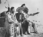 Teljes jelmezbe öltözött indiánok és cowboy szalmabálákon ülnek egy 1930-as évekbeli vadnyugati előadáson