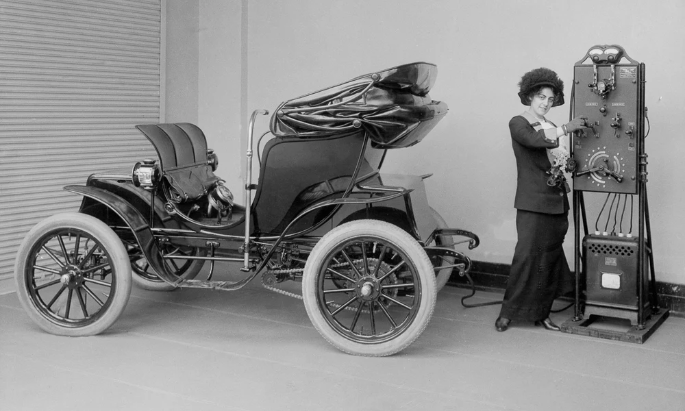 Egy asszony használja a kézi fogantyús akkumulátortöltőt a Columbia Mark 68 Victoria típusú automobil feltöltéséhez (1912 körül)