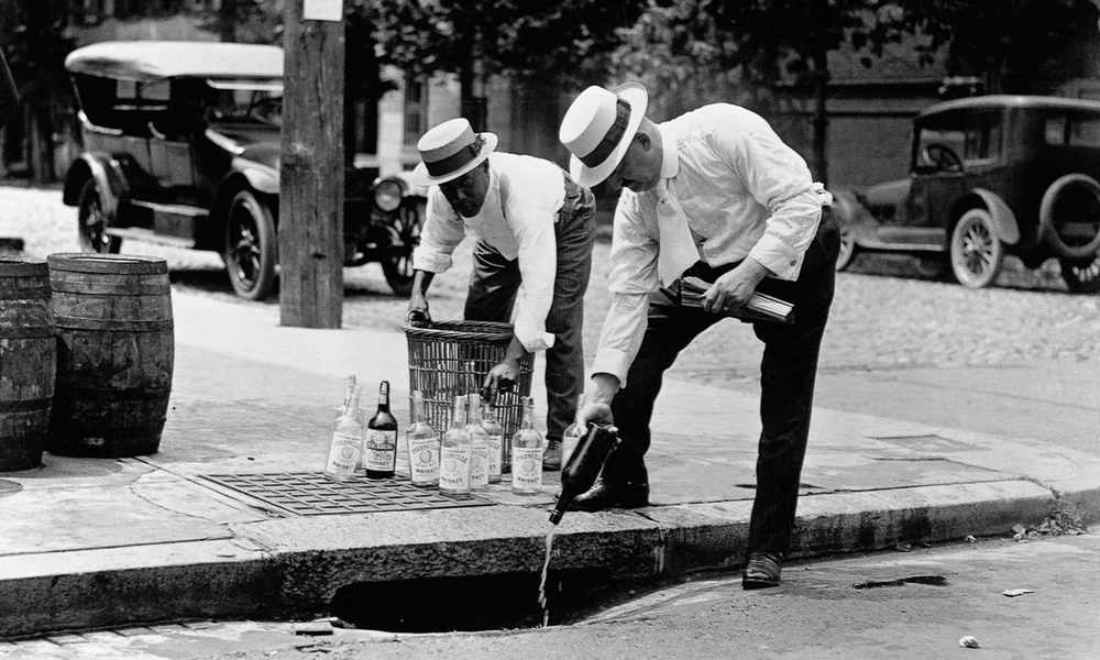 A bolttulajdonos saját maga önti a csatornába az alkoholos üvegeinek tartalmát (1920)