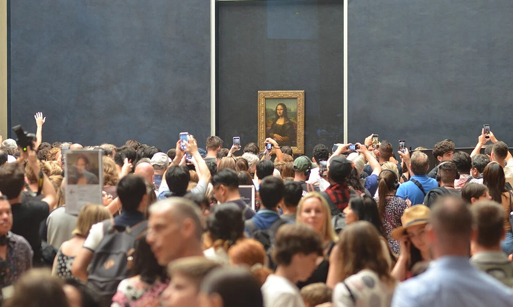 Látogatók tömege a Mona Lisa előtt a párizsi Louvre-ban (Forrás: Wikimedia Commons / Mosellaender (CC BY-SA 4.0))